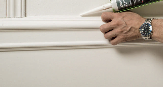 Akrylfog appliceras på en list på en vit vägg. 